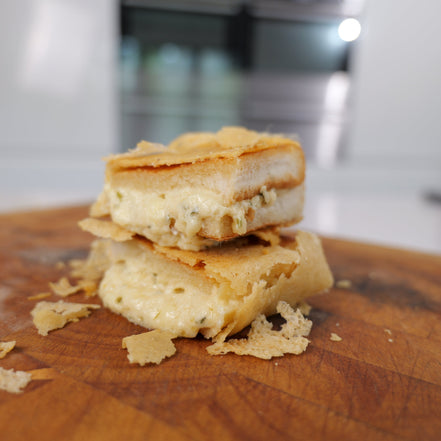 A cheese toasty with a parmesan crumb and melted cheese oozing out of the bread it is sandwiched between